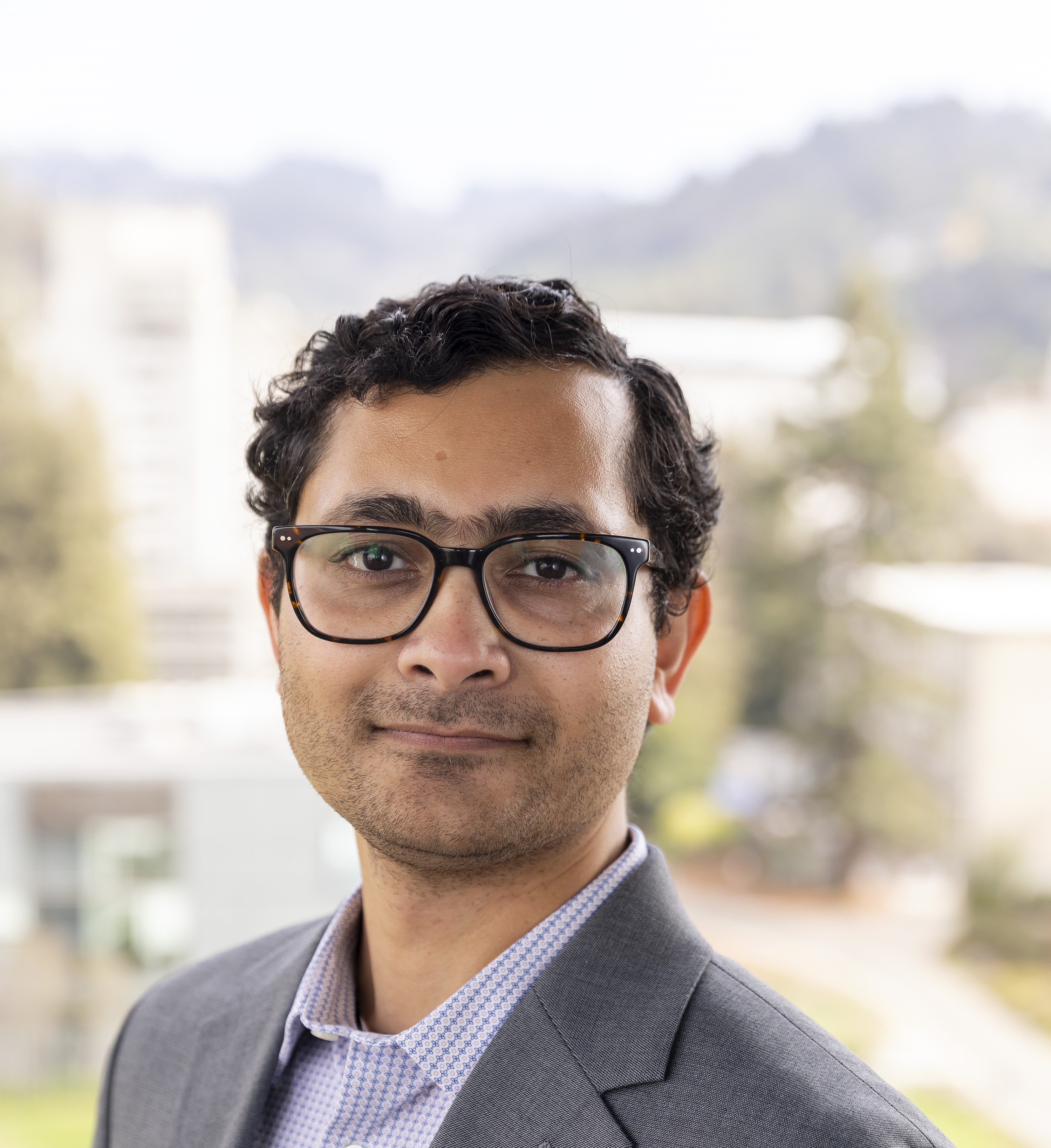 Anirvan Chowdhury, a man with curly hair and glasses, wearing a gray blazer, with a blurred background.